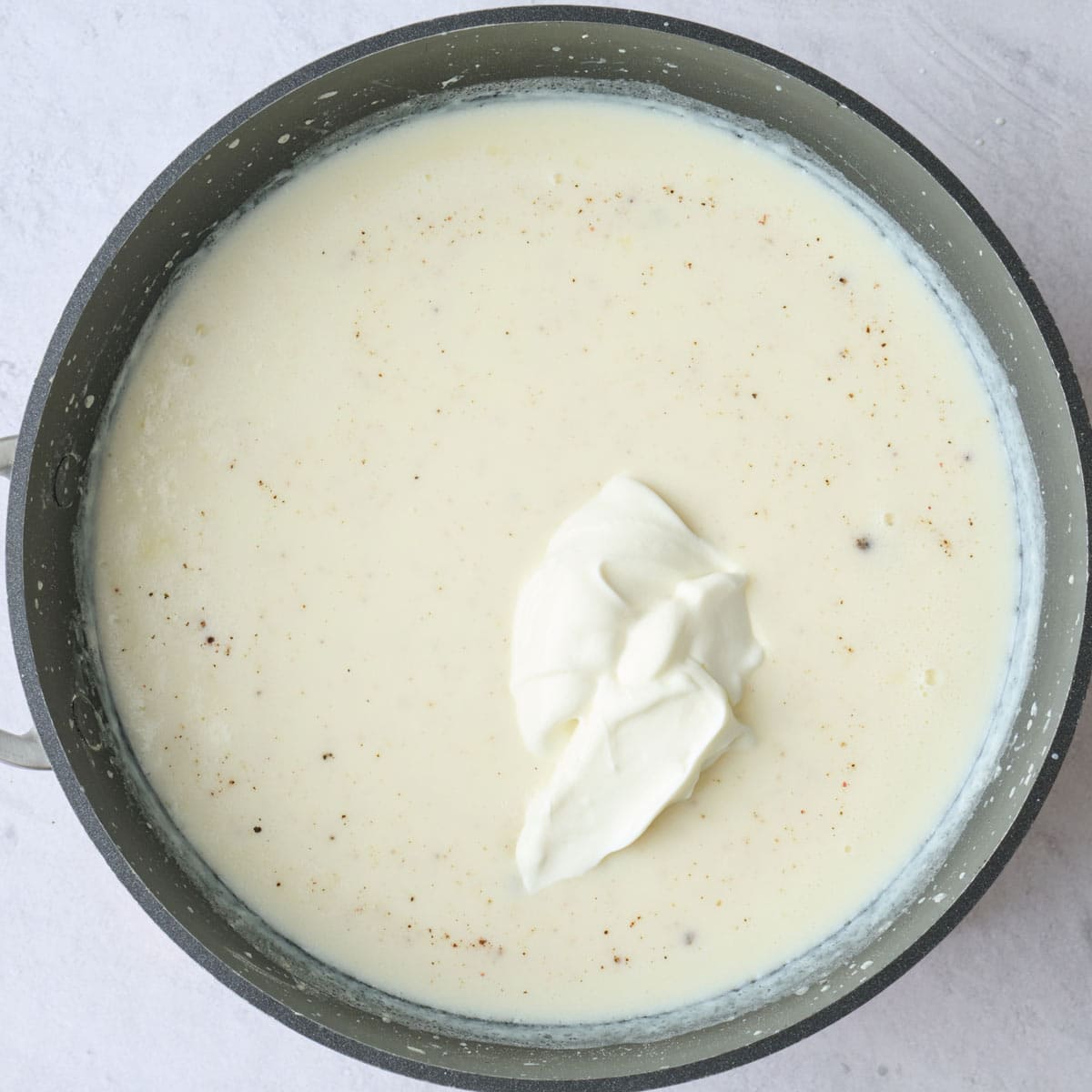 Thickened milk in a pan with greek yogurt added before mixing.