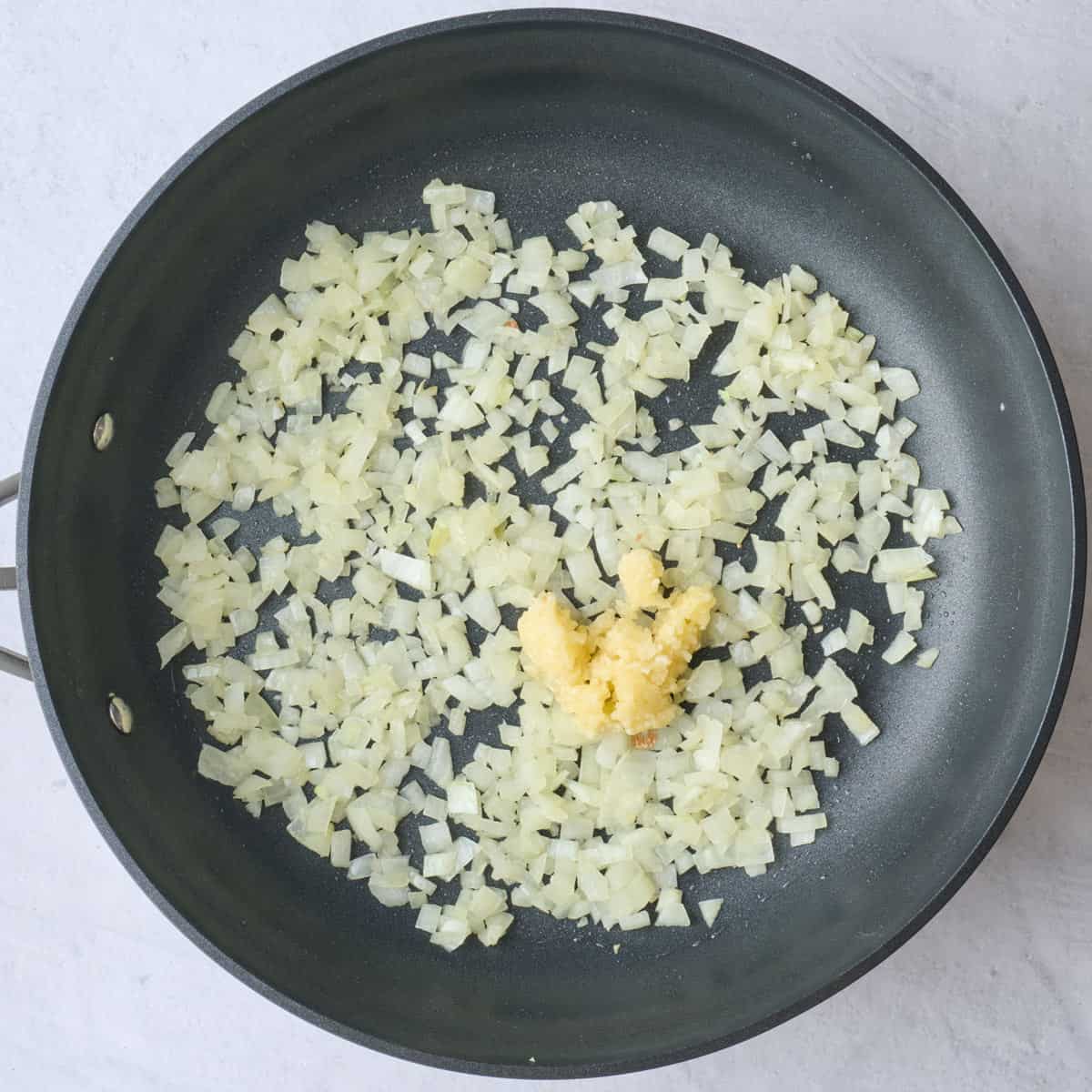 Cooked diced onions in a skillet with minced garlic added before cooking.