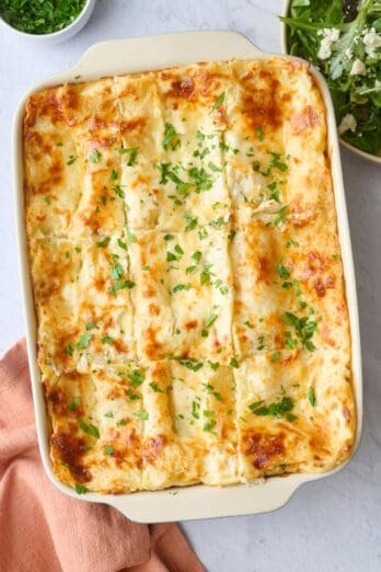 Chicken lasagna recipe in a baking dish cut into 9 servings and garnished with chopped parsley.