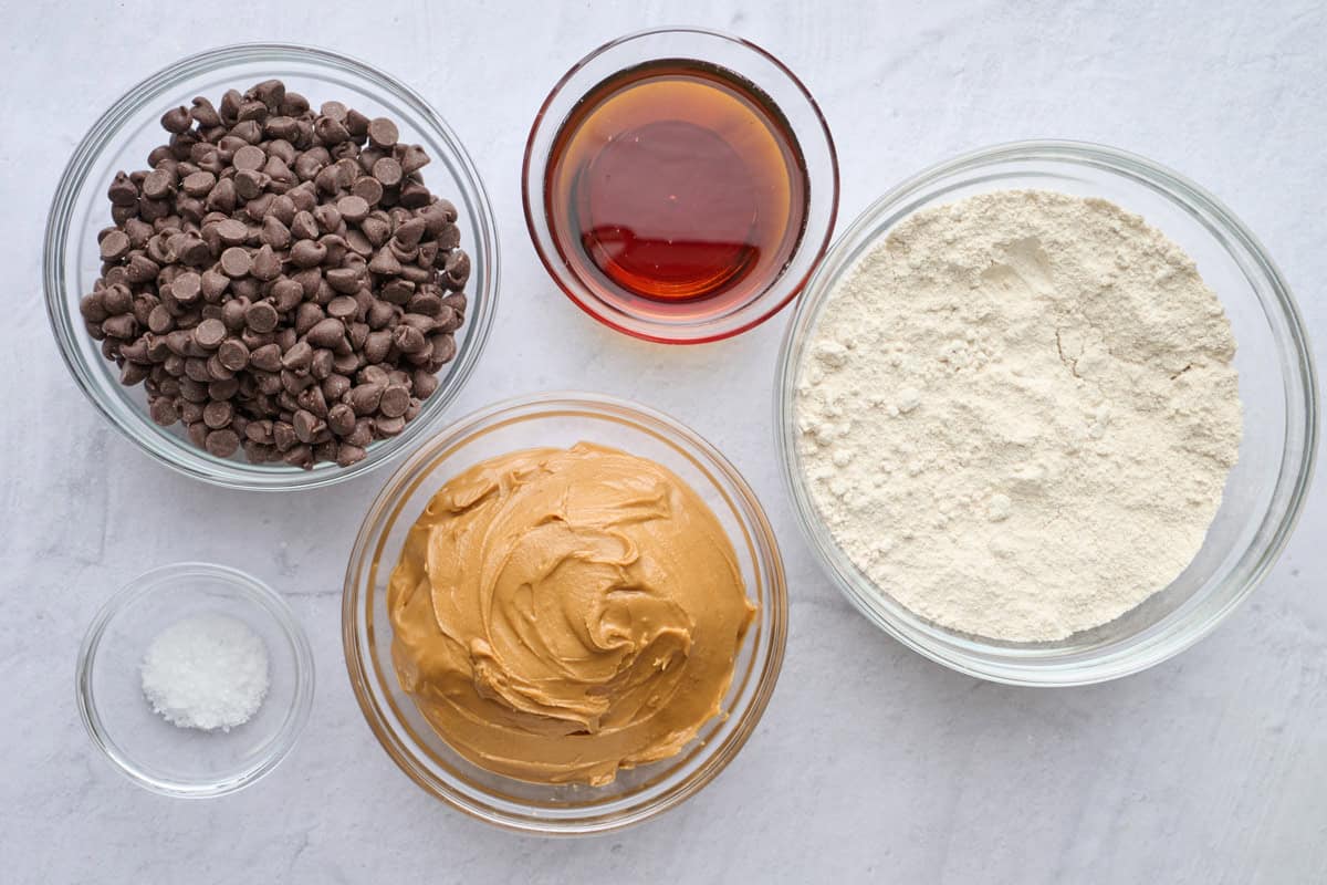 Ingredients for dessert bar recipe: chocolate chips, maple syrup, creamy peanut butter, oat flour, and flaky salt.