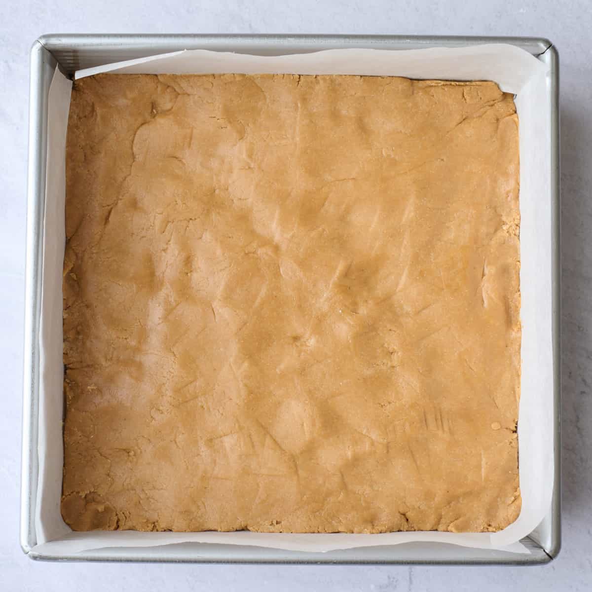 Peanut butter mixture pressed evenly into a parchment lined square pan for bar recipe.