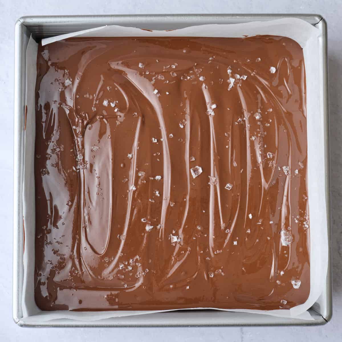 Melted pb chocolate mixture poured over dessert bar filling with salt sprinkled on top.