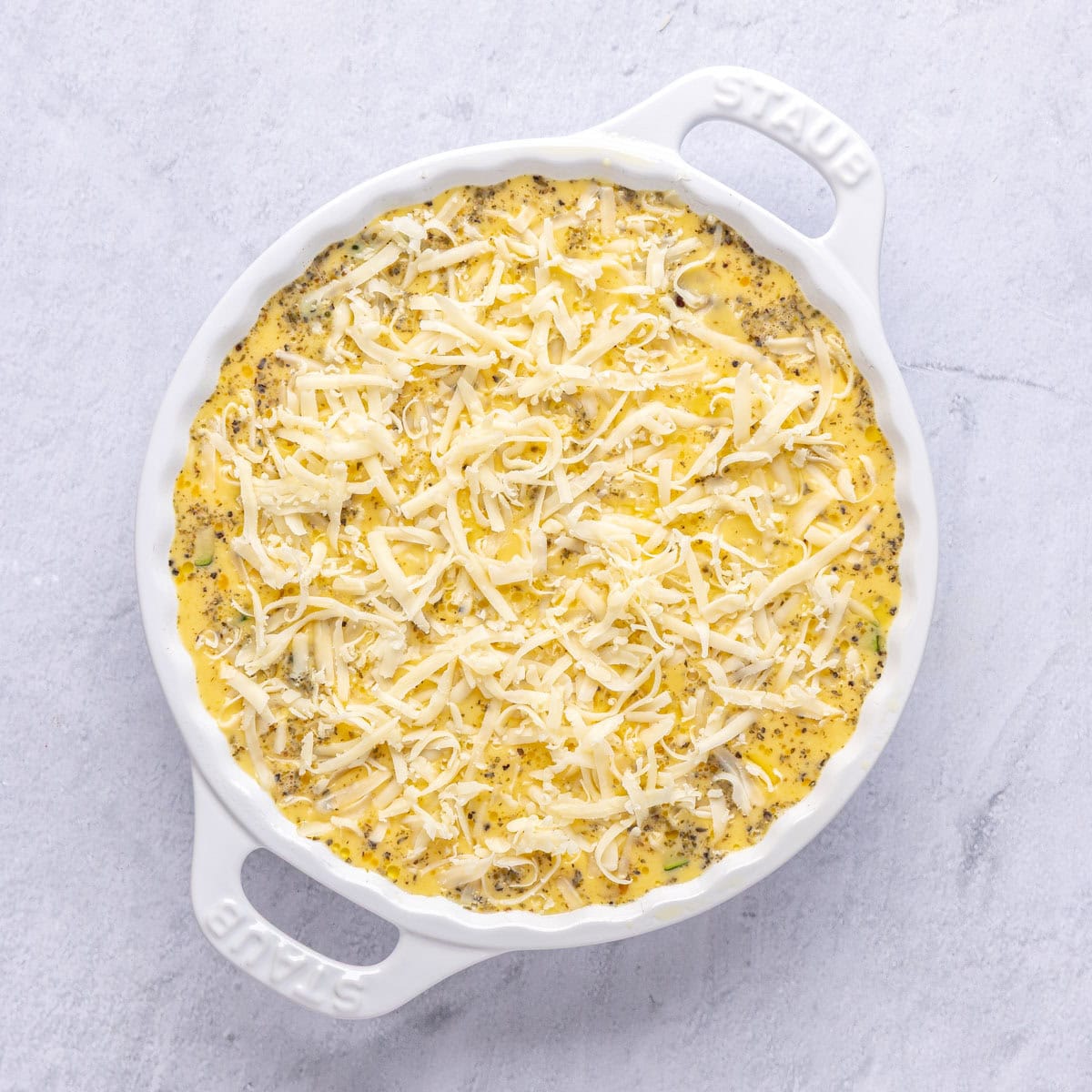 Eggs after whisked and poured on top of veggie cheese mixture with remaining cheese sprinkled on top for quich recipe before baking.