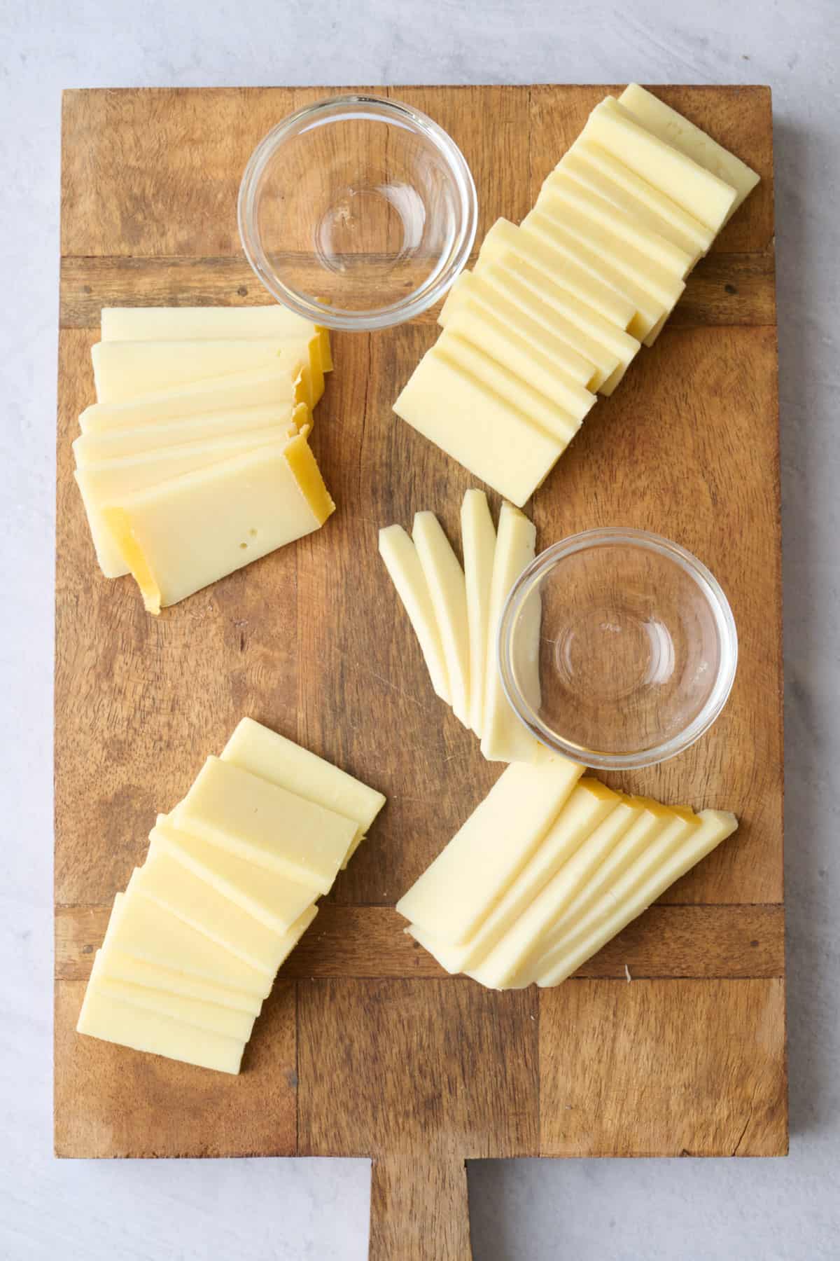 Cheese slices fanned out on a board with pinch bowls added for an appetizer platter.