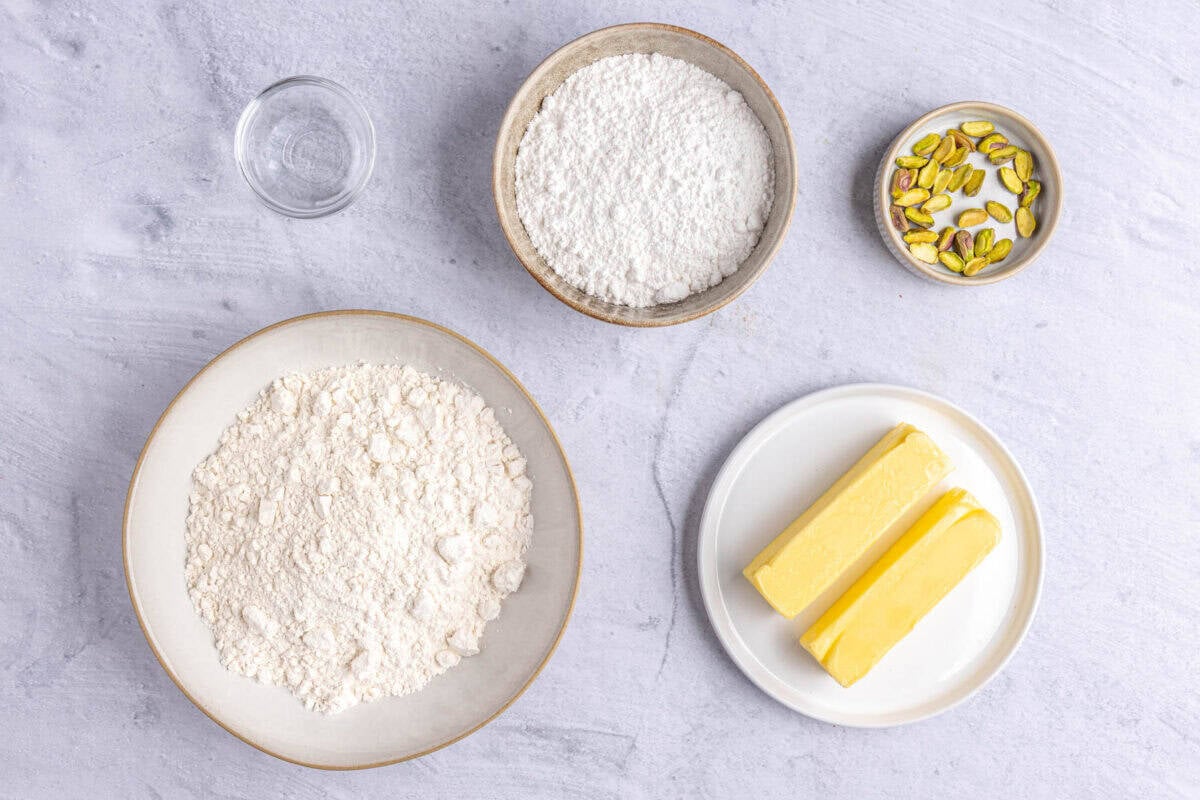 Ingredients for recipe; flour, rose water, powdered sugar, pistachios, and butter.