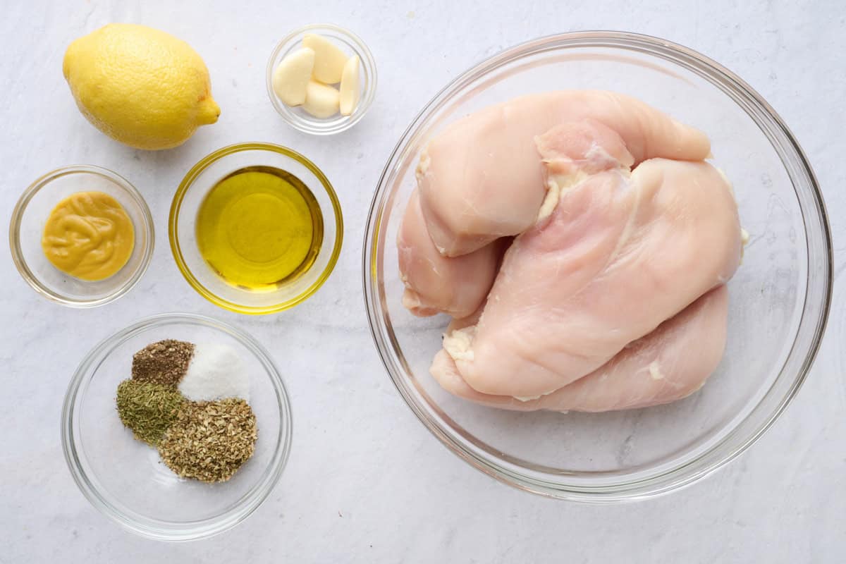 Ingredients for recipe: chicken breasts, lemon, Dijon mustard, seasonings, oil, and garlic cloves.