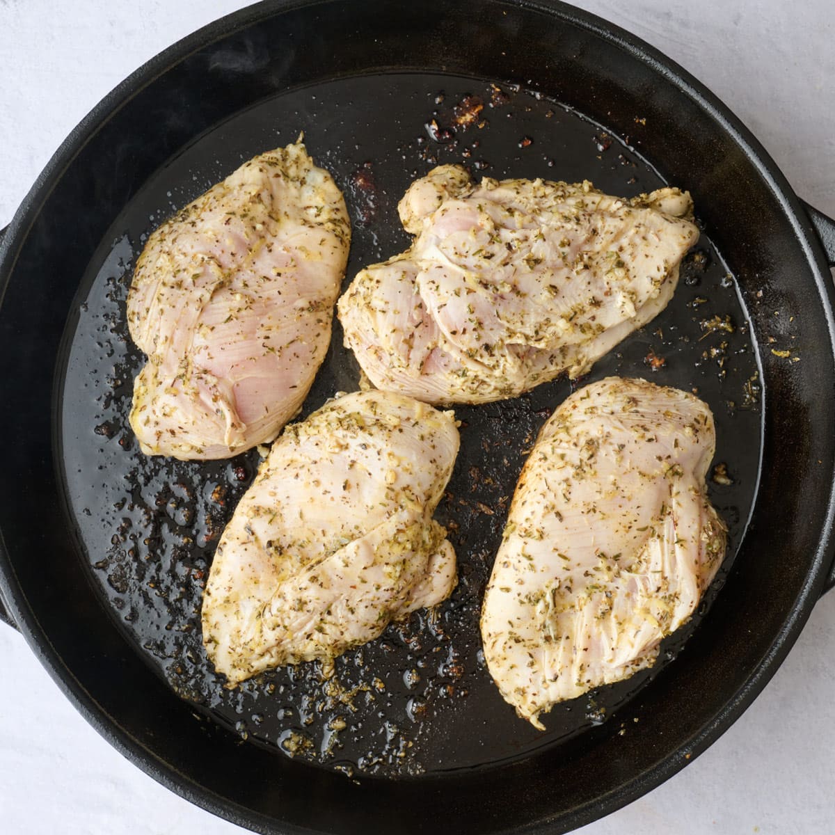 Marinated chicken breasts on a hot oiled skillet before cooking.