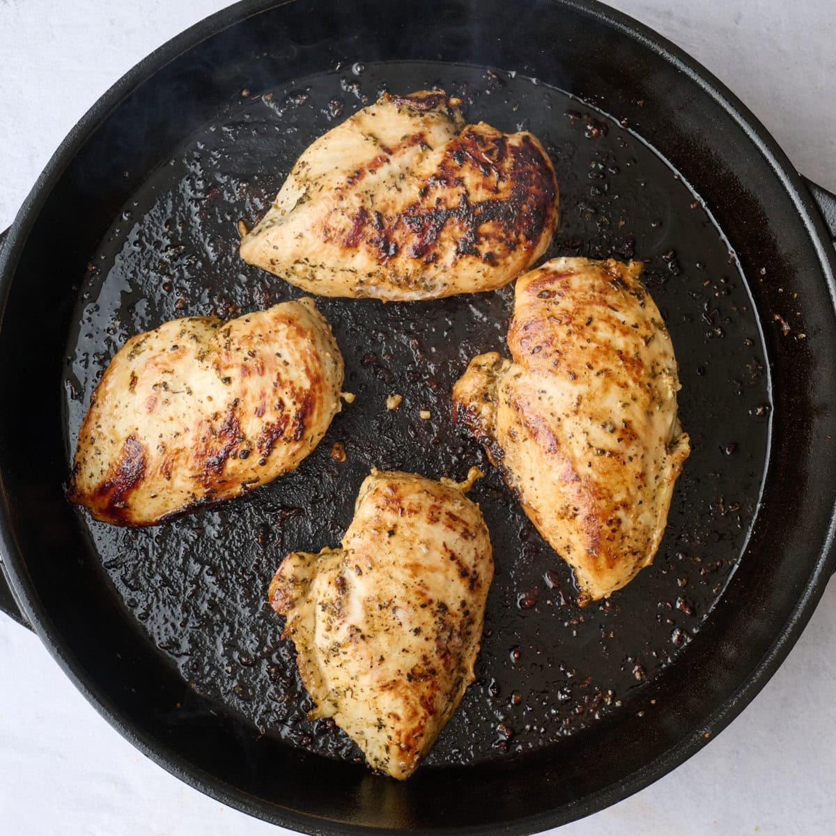 Pan cooked Greek chicken breasts after flipping.