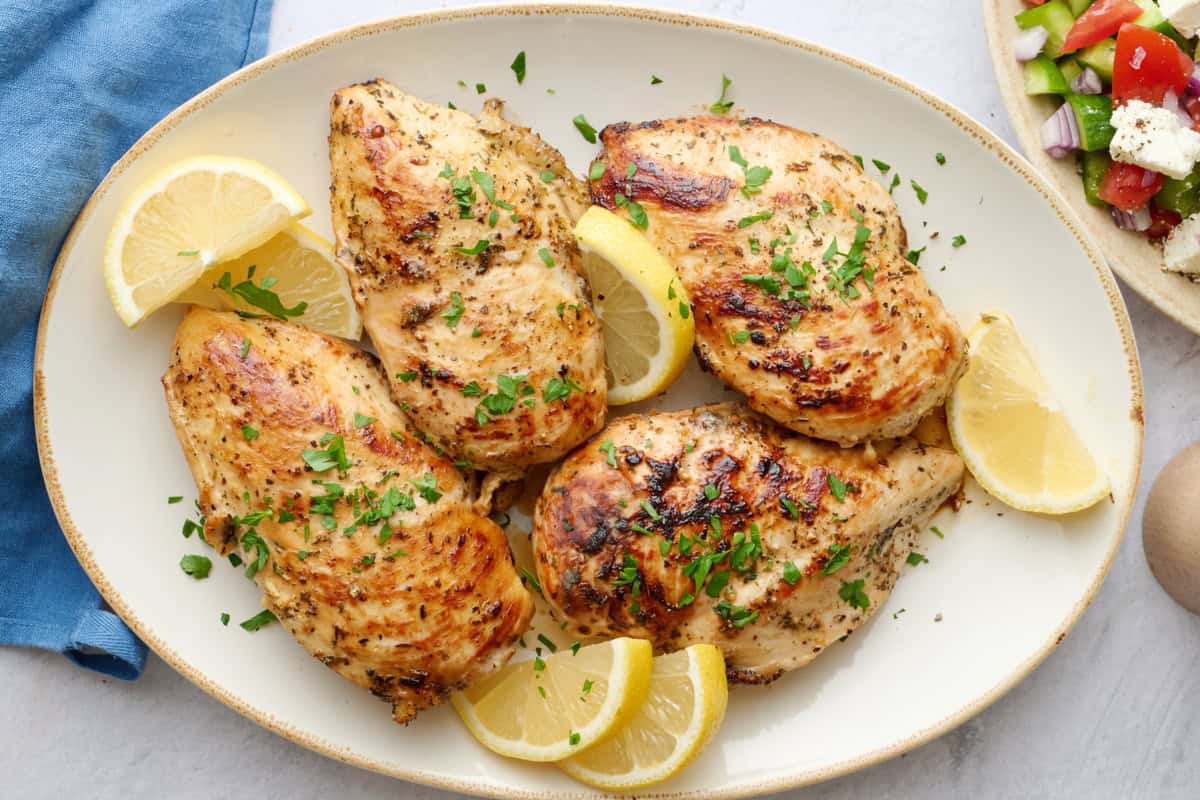 Easy Greek chicken breasts on a platter with lemon wedges.