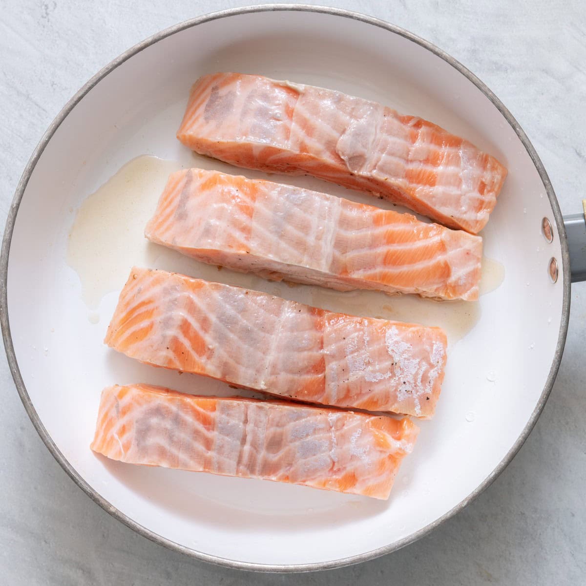 Four skin off salmon filets in an oiled skillet before cooking.