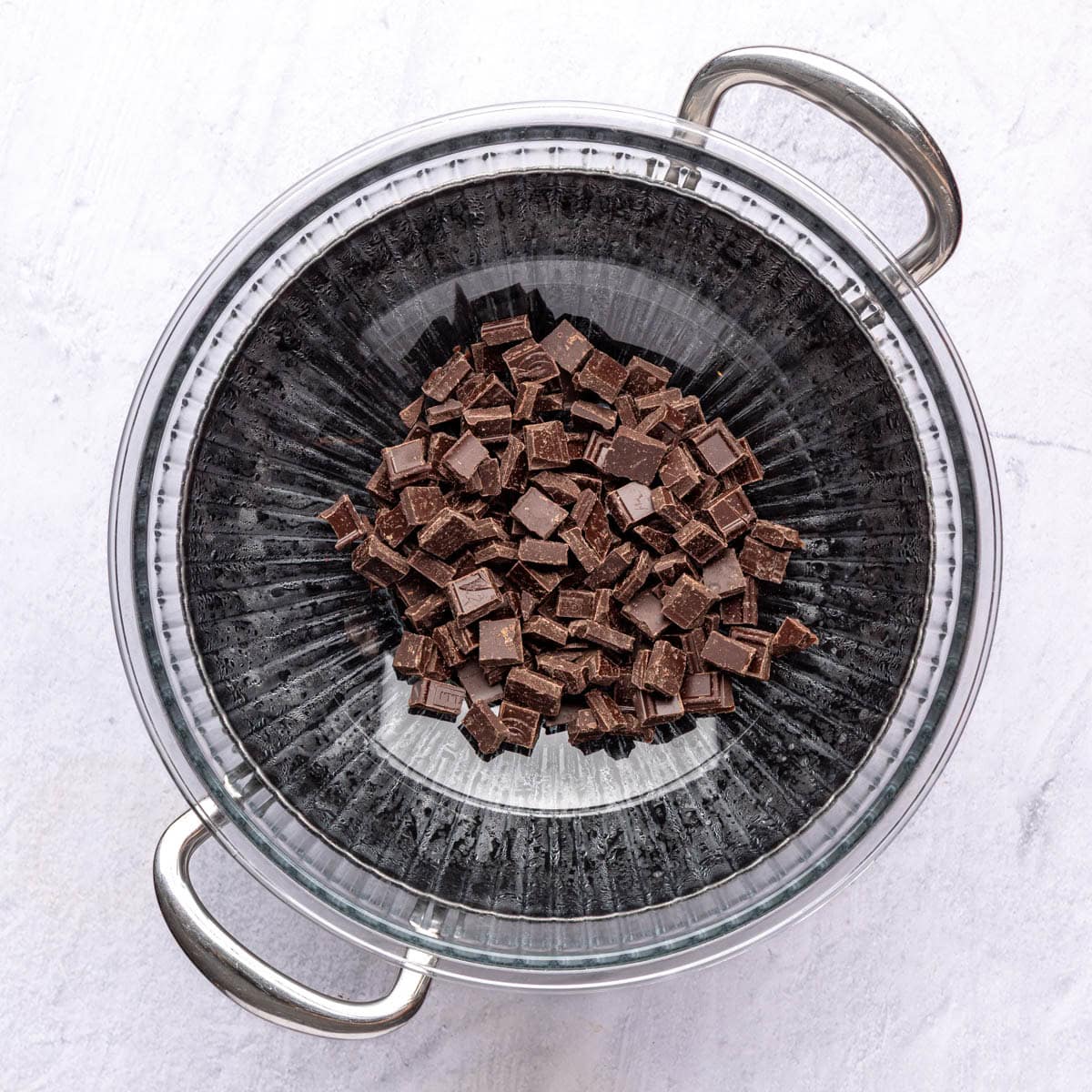 Chopped chocolate in bowl sitting on top of hot pot of water.