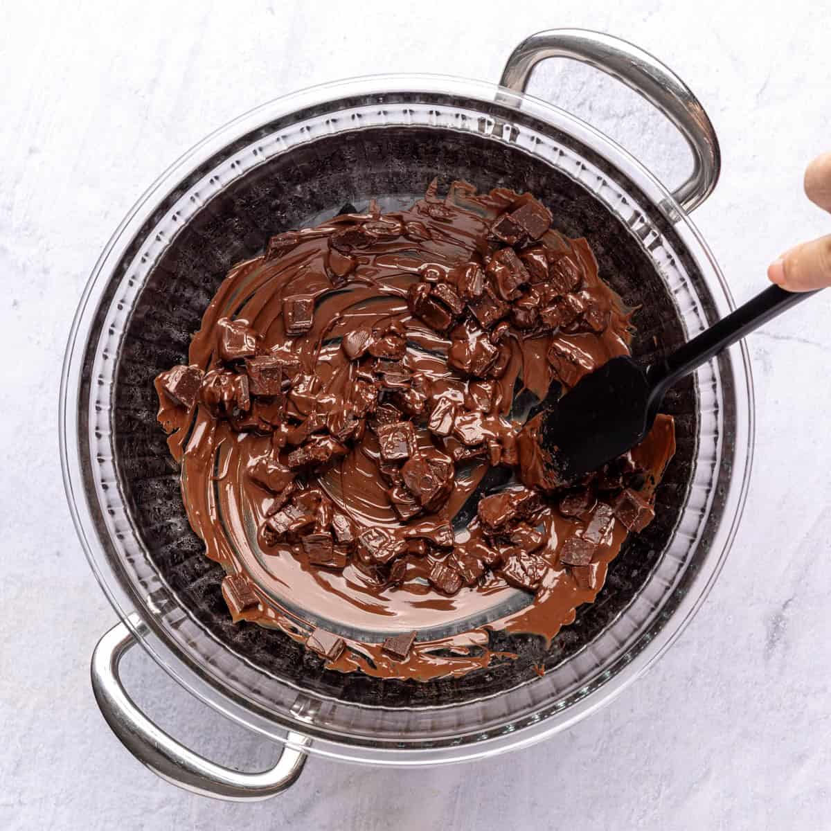 Rubber spatula stirring partially melted chocolate with some chunks still visible.
