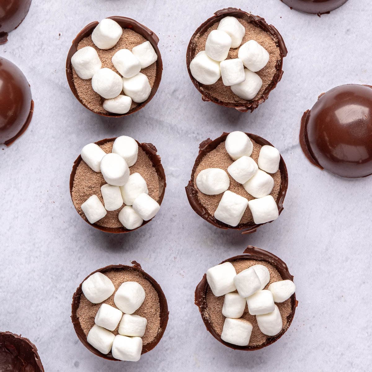 Marshmallows added on top of cocoa mix inside chocolate shells for cocoa bomb recipe.