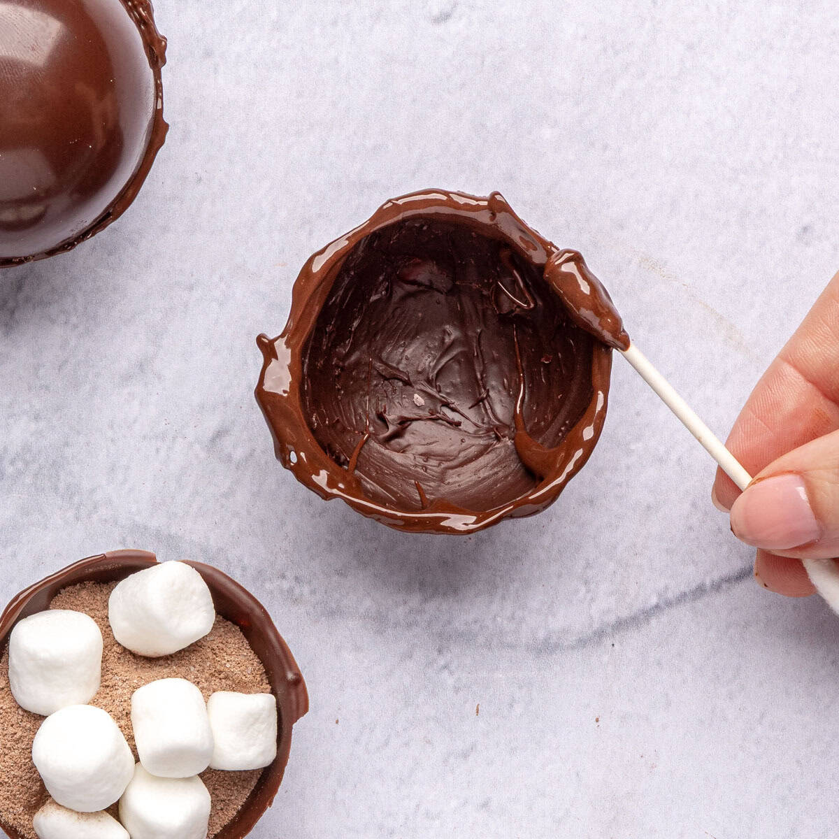 Melted chocolate being spread on edge of empty shell to seal cocoa bomb.
