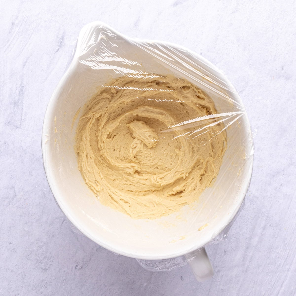 Cookie dough covered with plastic wrap to rest and chill before baking.