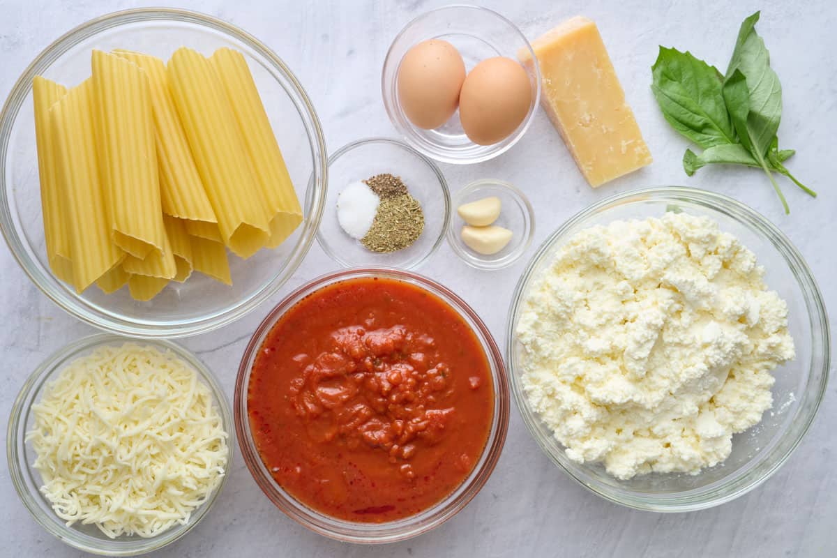 Ingredients for recipe: manicotti shells, eggs, ricotta cheese, shredded mozzarella cheese, parmesan, garlic cloves, basil, seasonings, and marinara sauce.
