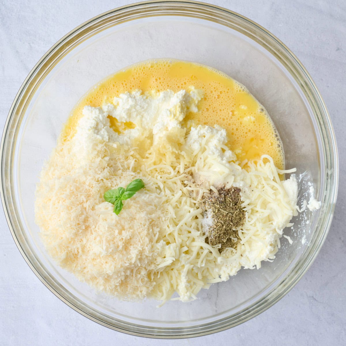 Whisked eggs in a bowl with ricotta, mozzarella, parmesan, garlic and seasonings added before mixing.