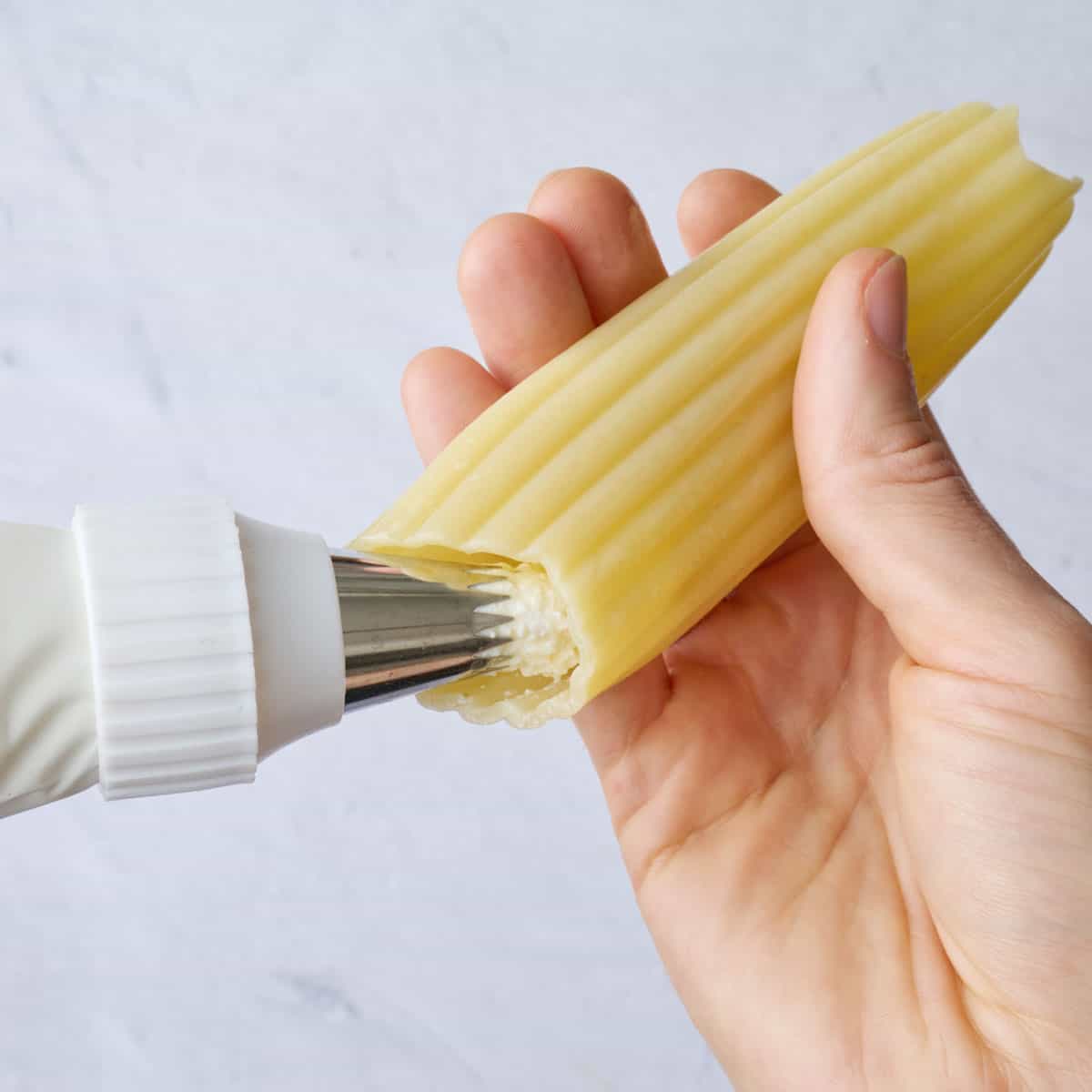 Piping cheese filling into a par cooked manicotti shell.