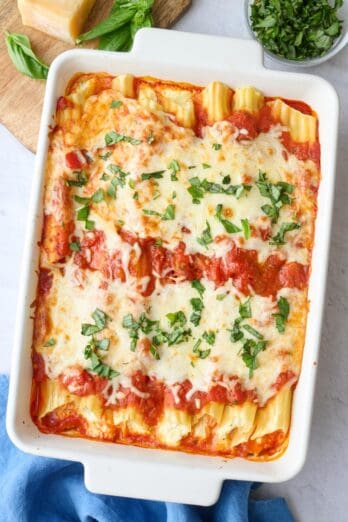 Homemade manicotti recipe in a baking dish garnished with fresh basil.
