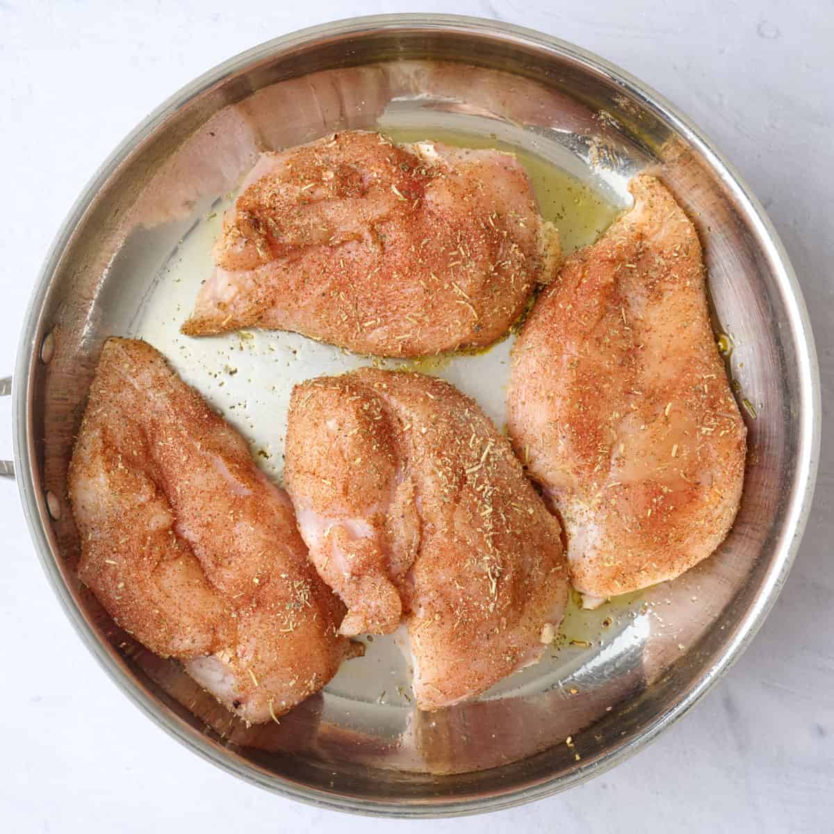 Seasoned chicken breast added to an oiled skillet before cooking.