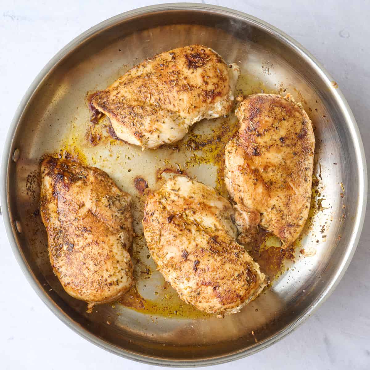 Seasoned chicken breasts after cooking in a skillet for recipe.