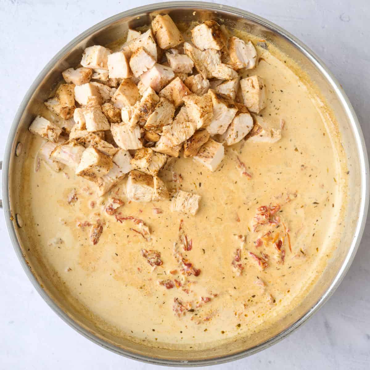 Diced cooked chicken breasts added on top of the creamy sun-dried tomato sauce before combining.