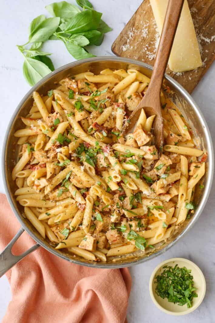 Marry me pasta with chicken in a skillet with a wooden serving spoon dipped inside, garnished with extra chopped basil and grated parmesan.