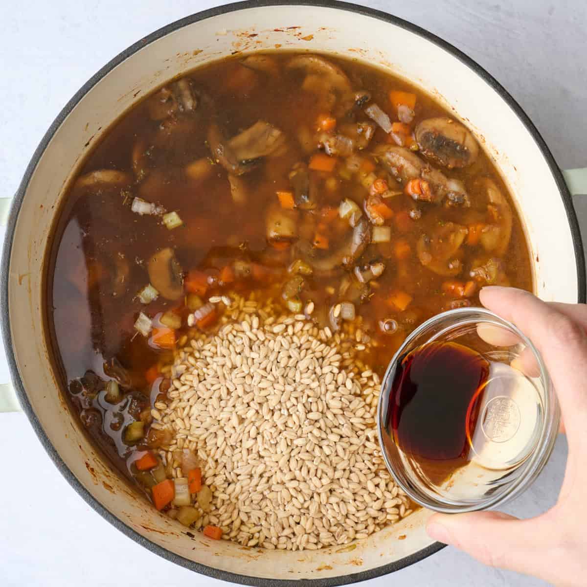 Barley, broth and soy sauce added to soup pot before combining.