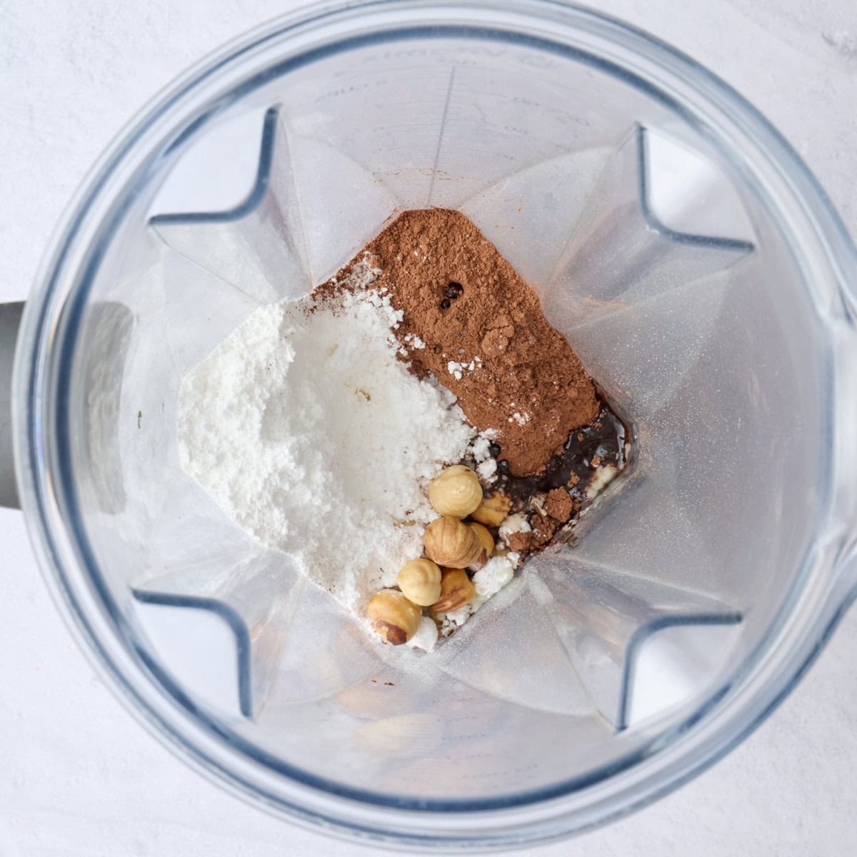 Skinned roasted hazelnuts, powdered sugar, cocoa powder, oil, vanilla, and salt in a blender before blending.