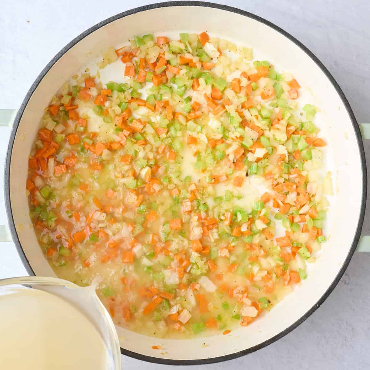 Cooked mirepoix with broth being poured into pot.