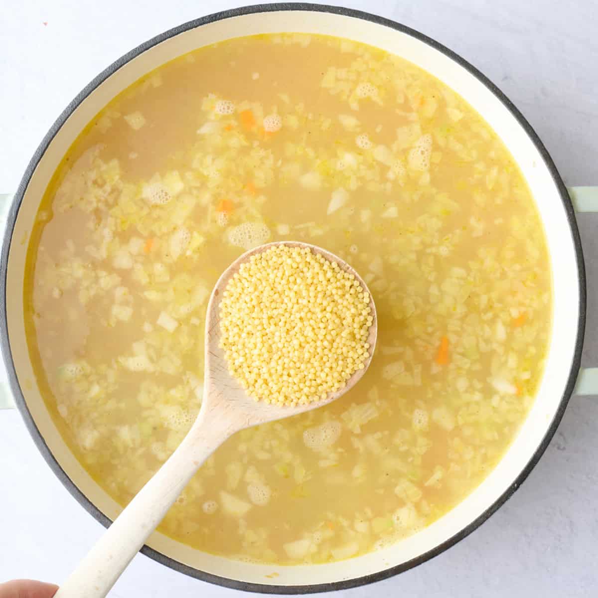 Uncooked Acini di Pepe (pastina) being added to pot of soup.