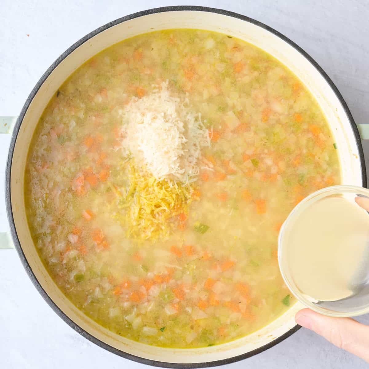 Grated parmesan and lemon zest added to soup pot with lemon juice being poured in.