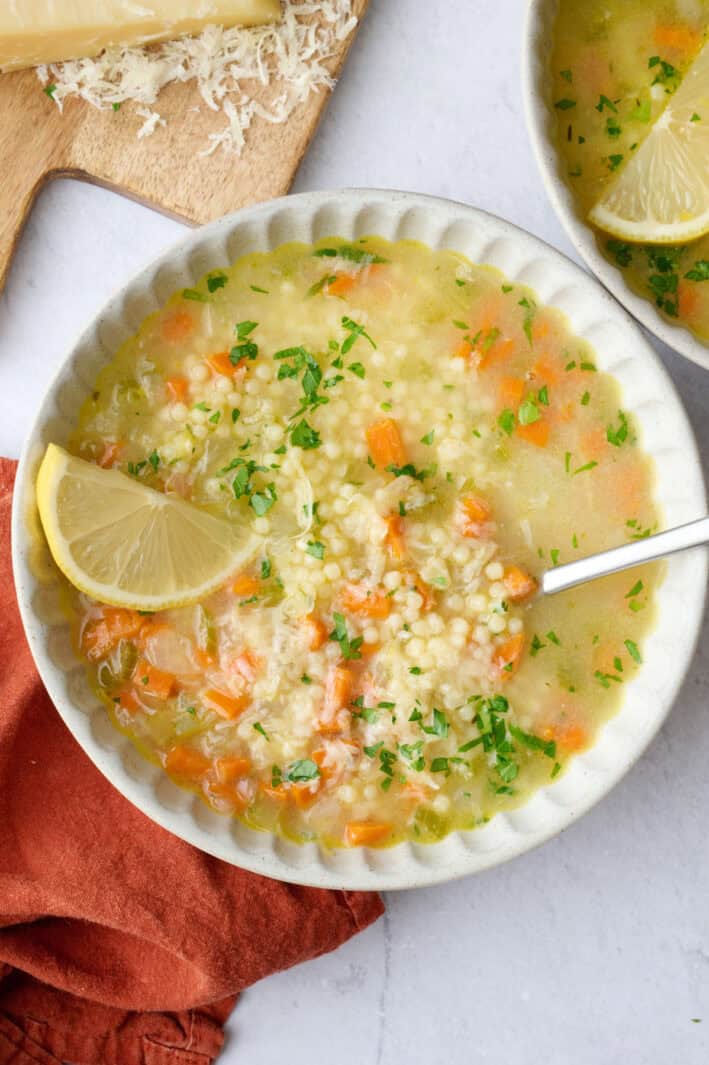 Two bowls of homemade pastina soup garnished with extra parmesan cheese, lemon and chopped parsley.