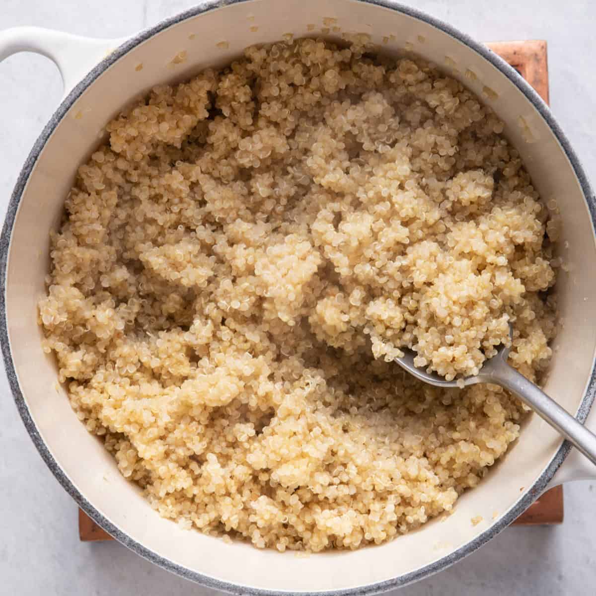 Cooked quinoa in a pot with a spoon lifting some up.