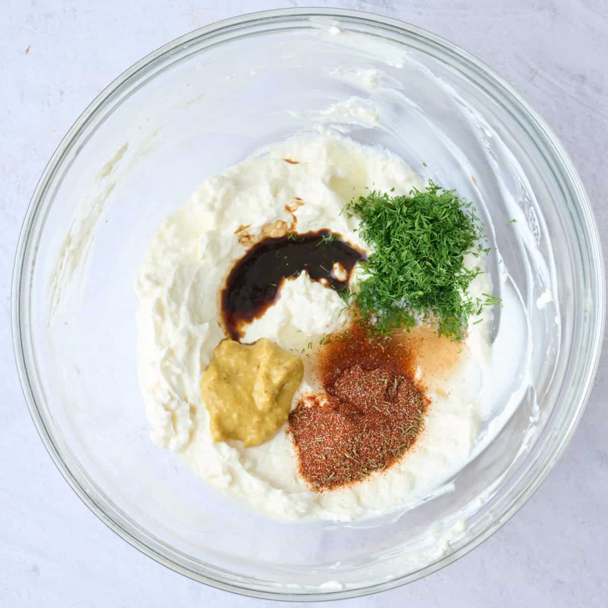 Greek yogurt and cream cheese mixture in a bowl with lemon juice, dijon, dill, Worcestershire, old bay and garlic powder added before mixing.