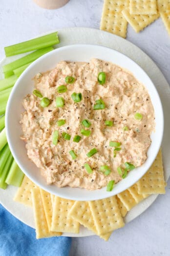 Shrimp dip with cream cheese served in a bowl with crackers and celery for dipping.