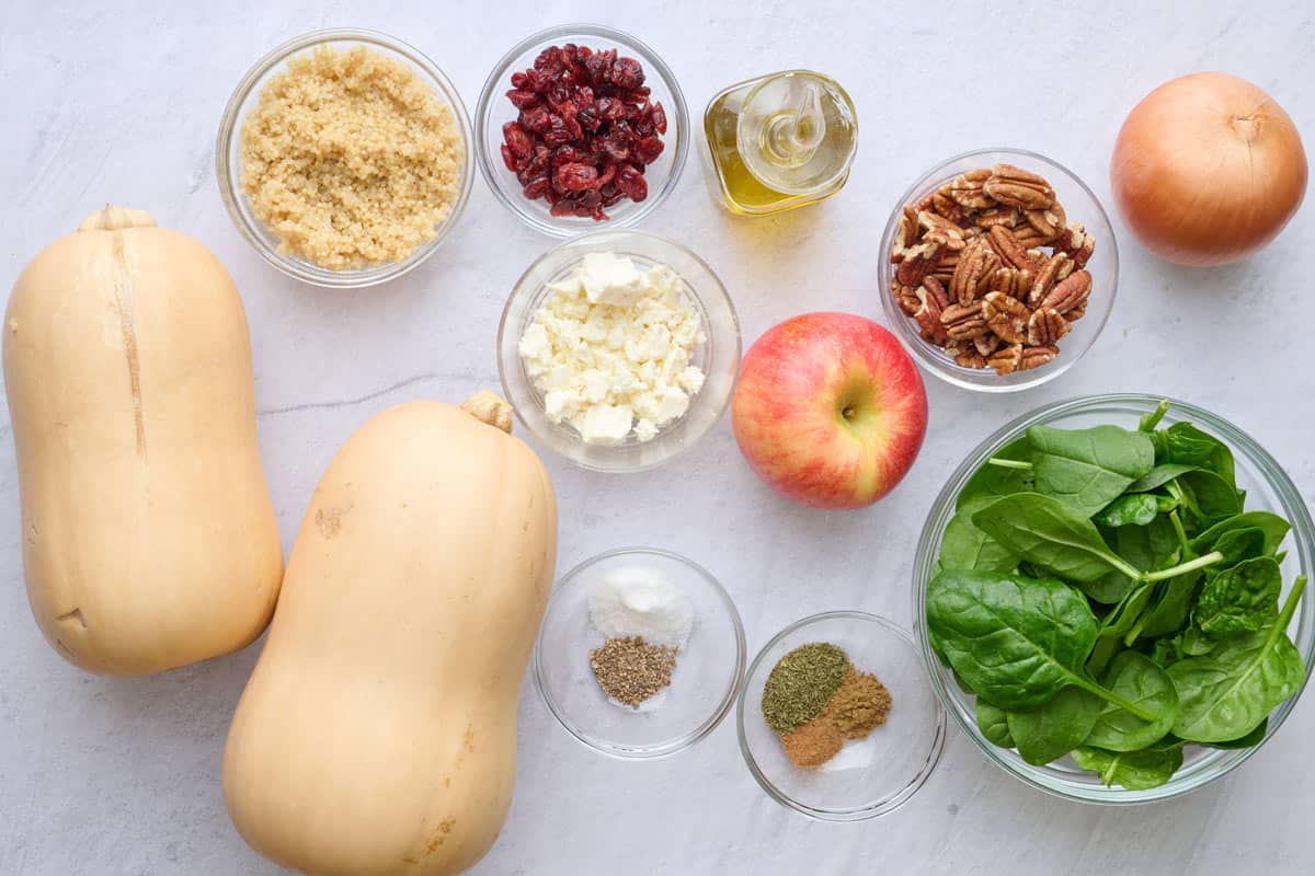 Ingredients for vegetarian dinner recipe: butternut squash, cooked quinoa, dried cranberries, feta cheese, oil, apple, pecans, seasonings, spinach and onion.