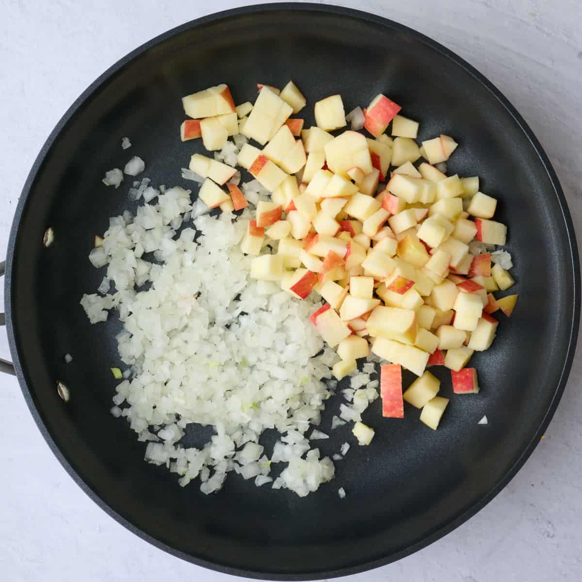 Diced apples and onions in a skillet before cooking for stuffed squash filling.