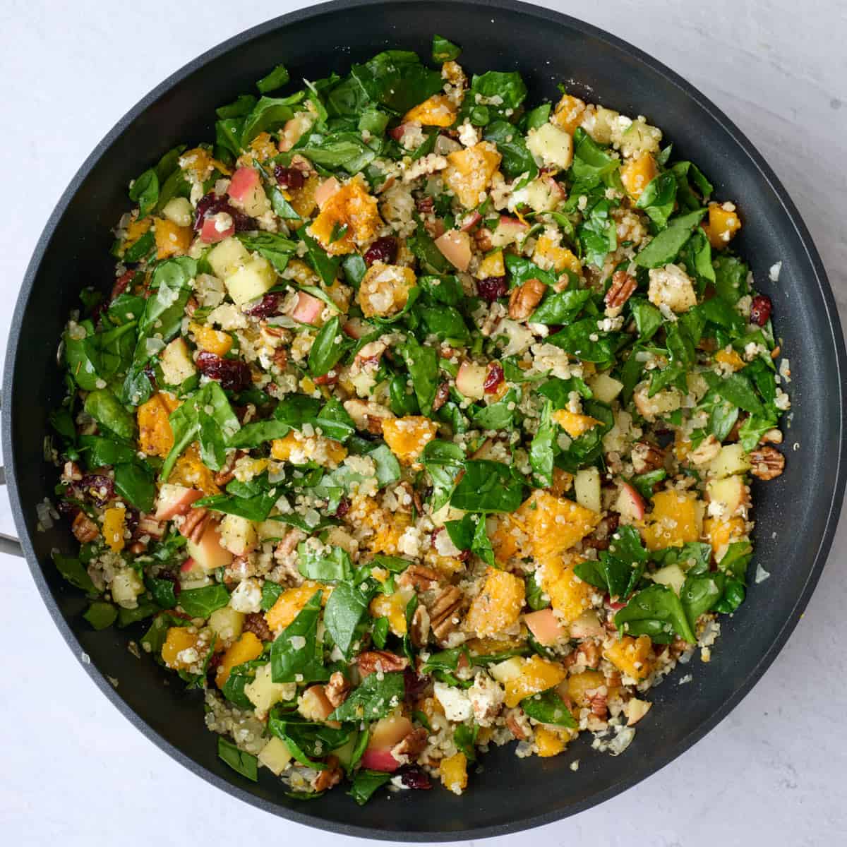 Quinoa, pecan, spinach and cranberry filling with feta cheese in skillet with butternut squash pieces.