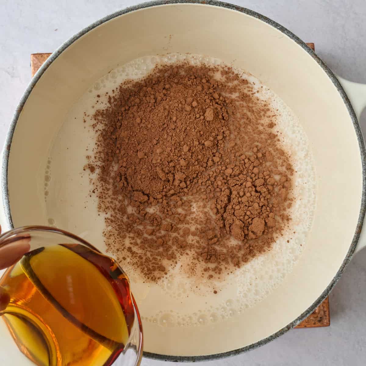 Almond milk, cocoa powder and maple syrup in a sauce pan before whisking for hot chocolate recipe.