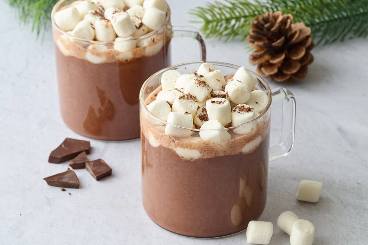 Two glass mugs of vegan hot chocolate made with almond milk and topped with mini marshmallows and chocolate shavings,