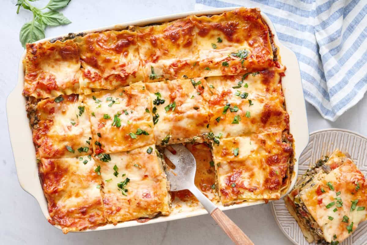 Easy vegetable lasagna recipe in a baking dish with a serving on a small plate to the side.