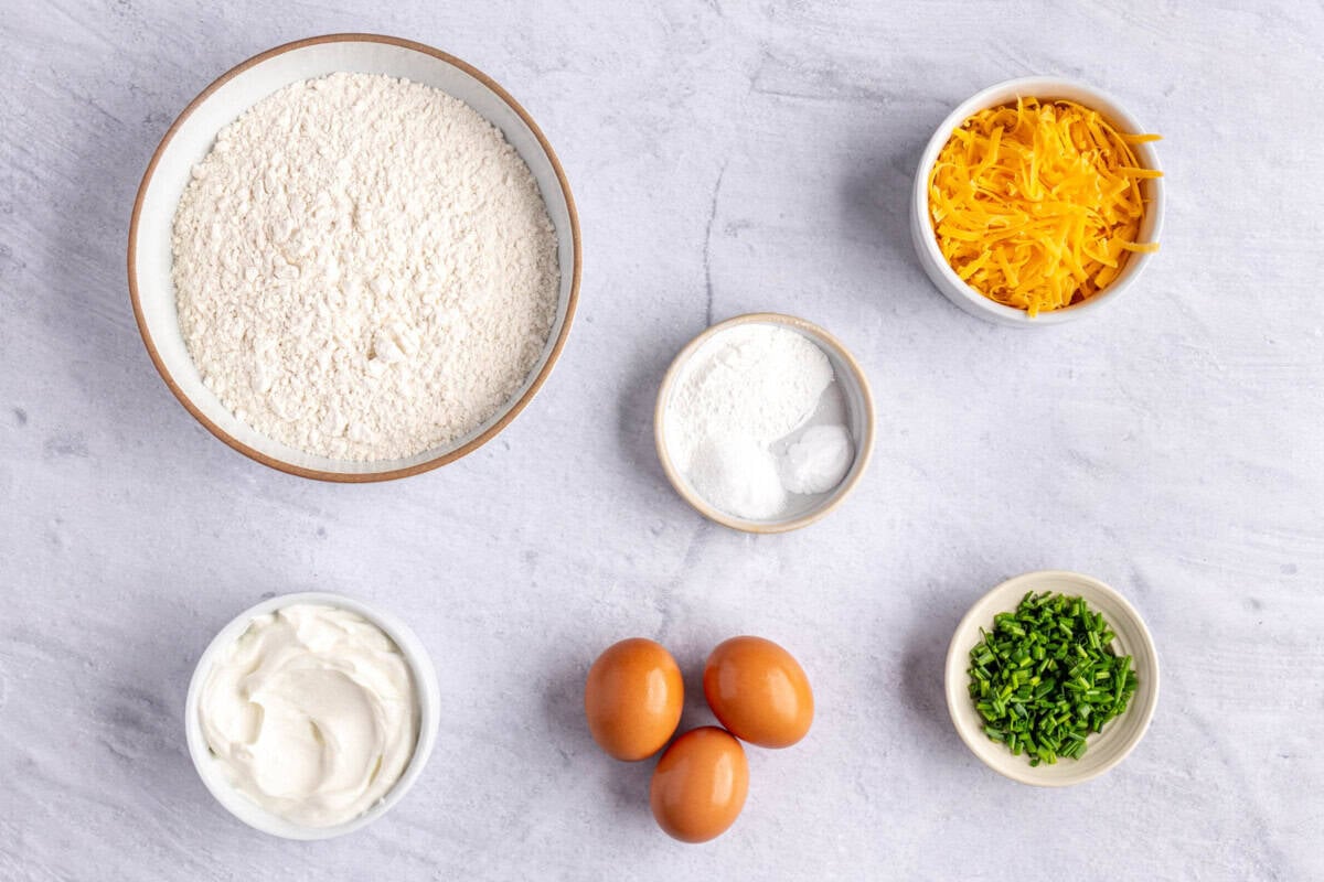 Ingredients for biscuit recipe: flour, Greek yogurt, eggs, cheese, chives, baking powder baking soda, and salt.