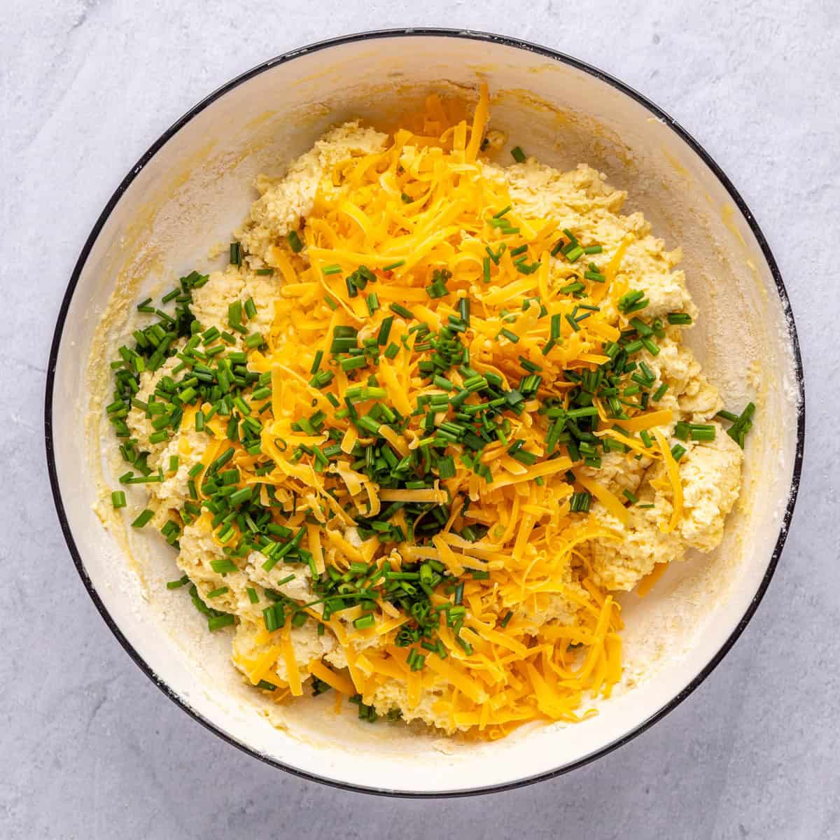 Wet and dry ingredients folded together with shredded cheddar cheese and chives added on top before folding into biscuit dough.