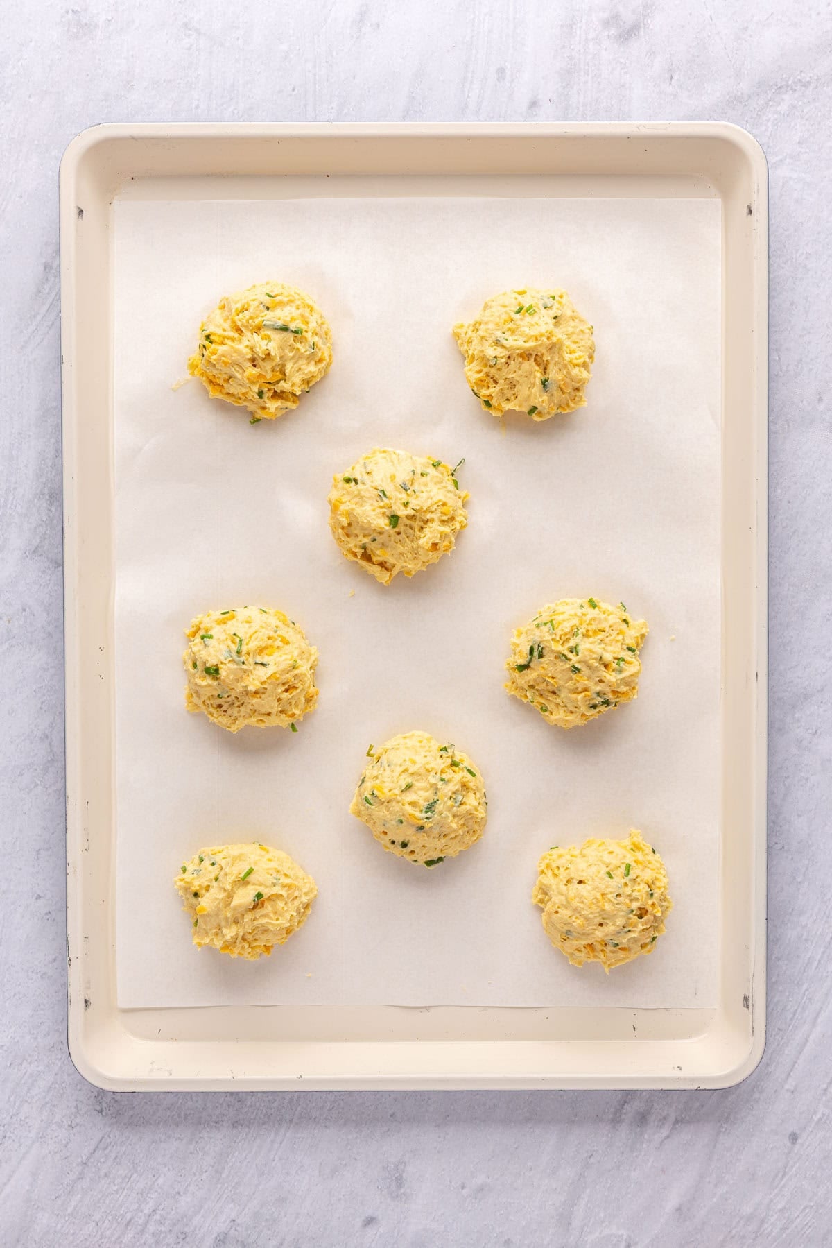 8 mounds of biscuit dough on a parchment lined baking sheet before baking.
