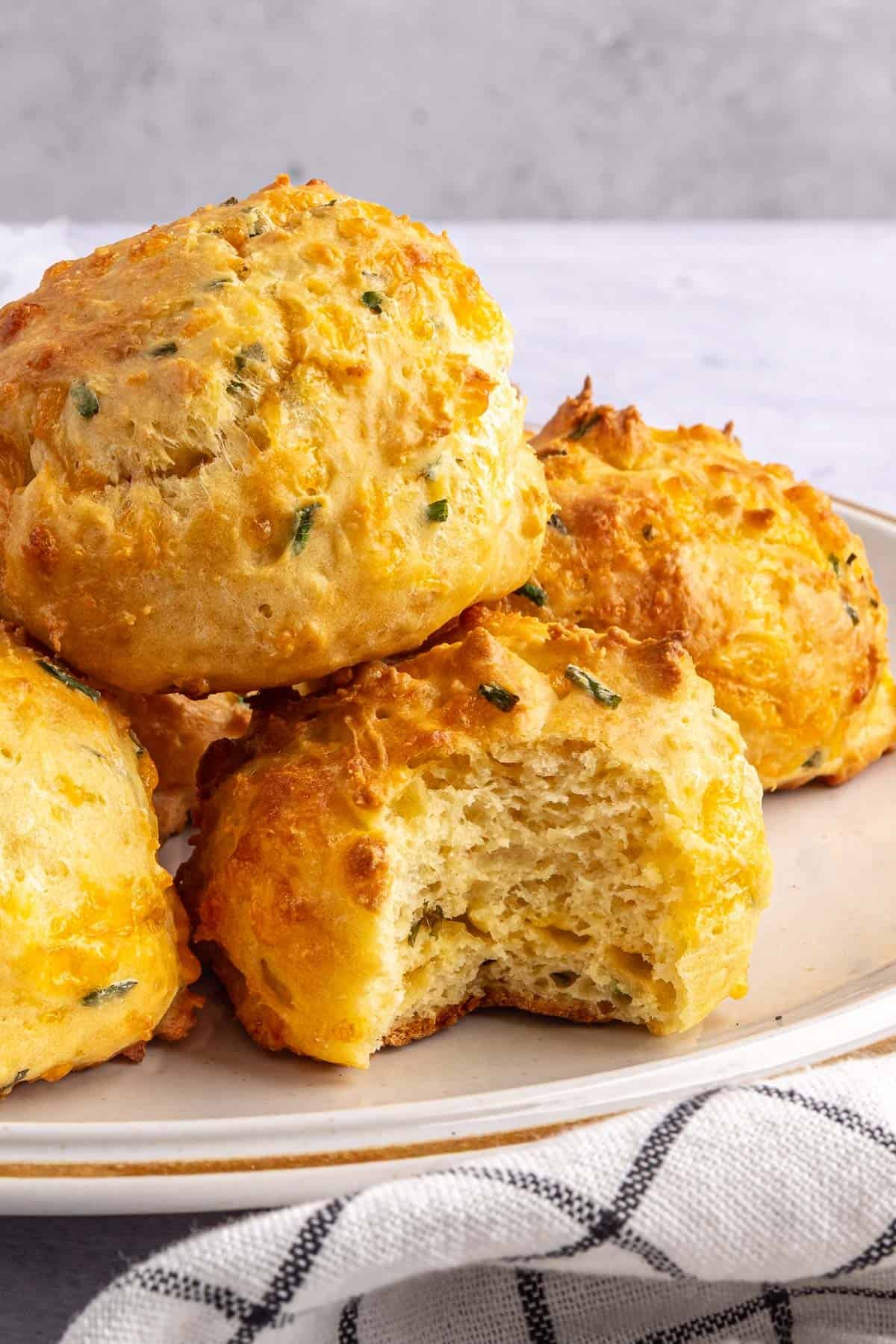 Best breakfast biscuits made with eggs, cheese and chives stacked on a plate with a bite taken out to show fluffy texture inside.
