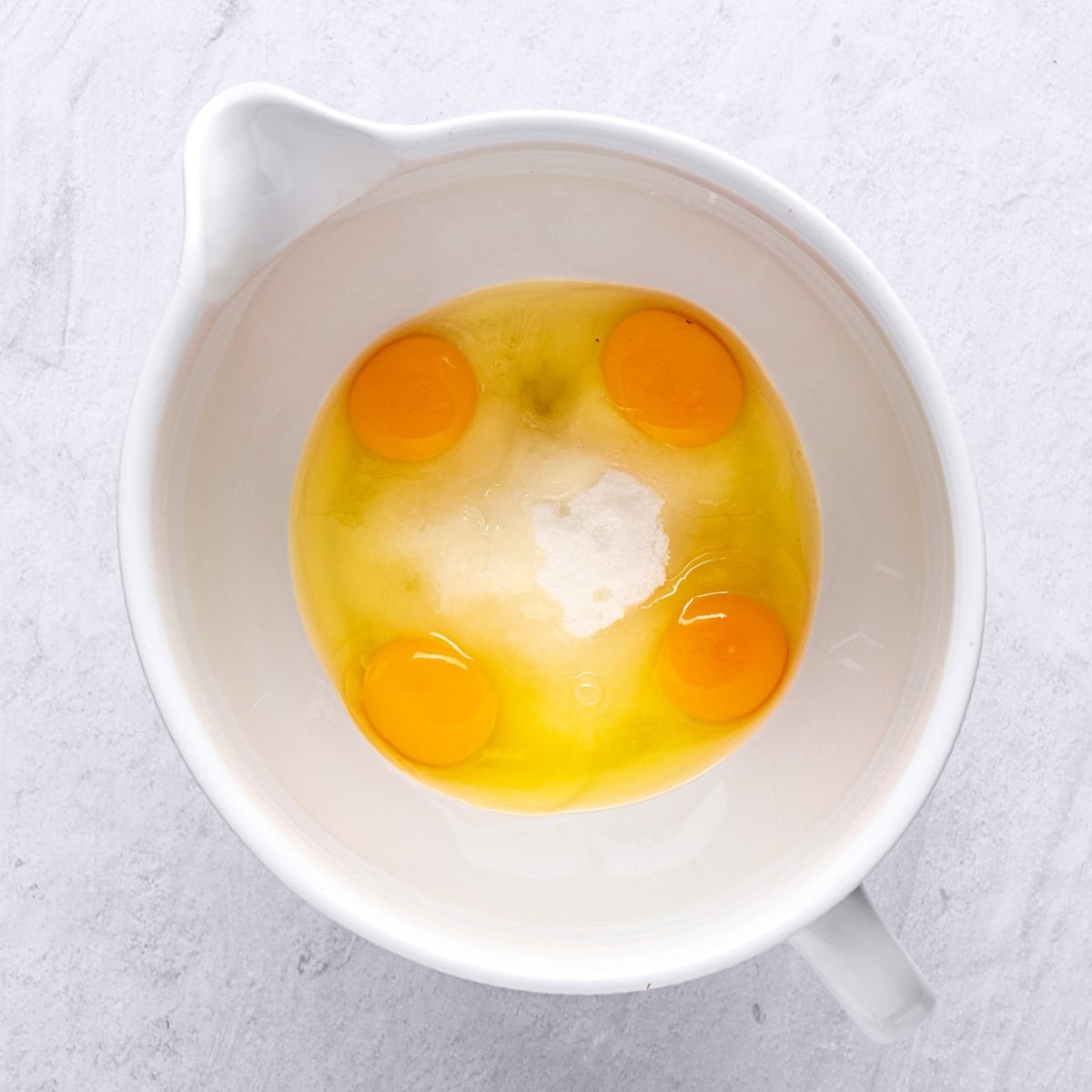 Eggs and sugar in the bowl of a stand mixer before beating.