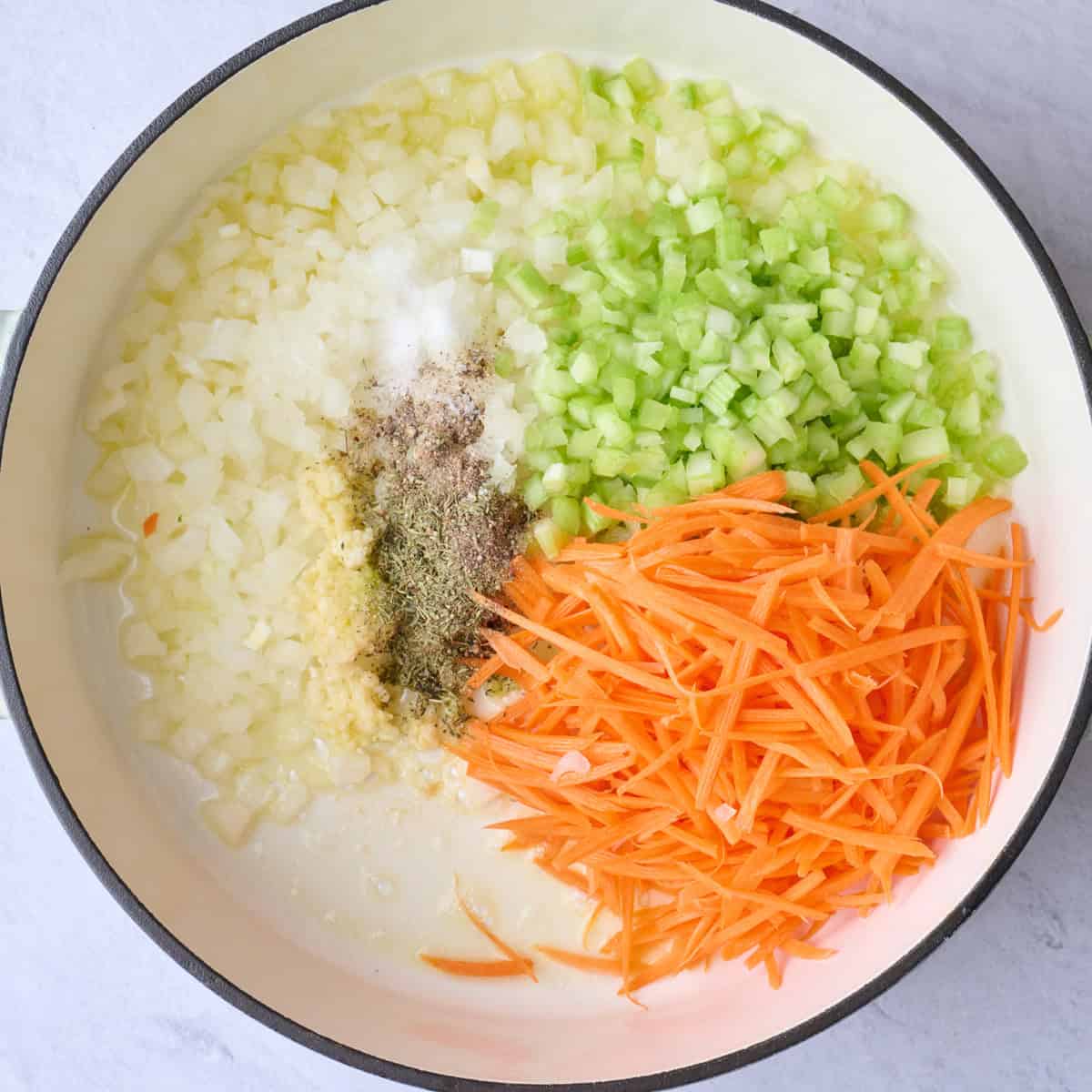 Onion, celery and shredded carrots in a pot of cooking with garlic, salt pepper and thyme added.