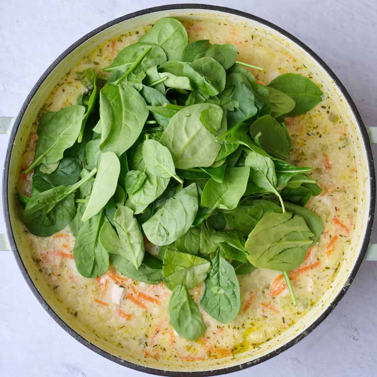 Spinach added on top of chicken gnocchi soup with milk recipe in pot before stirring in.