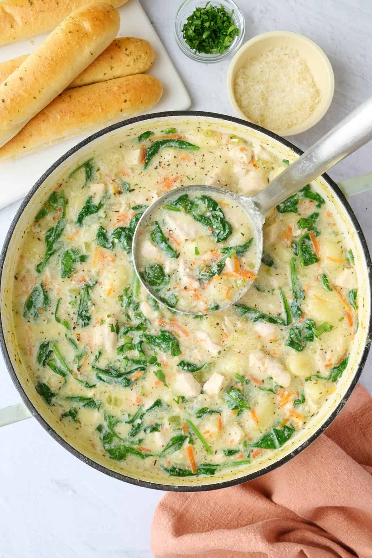 Best chicken gnocchi soup recipe in a pot with a ladle lifting some up, small dishes of parmesan and parsley nearby with breadsticks for serving.